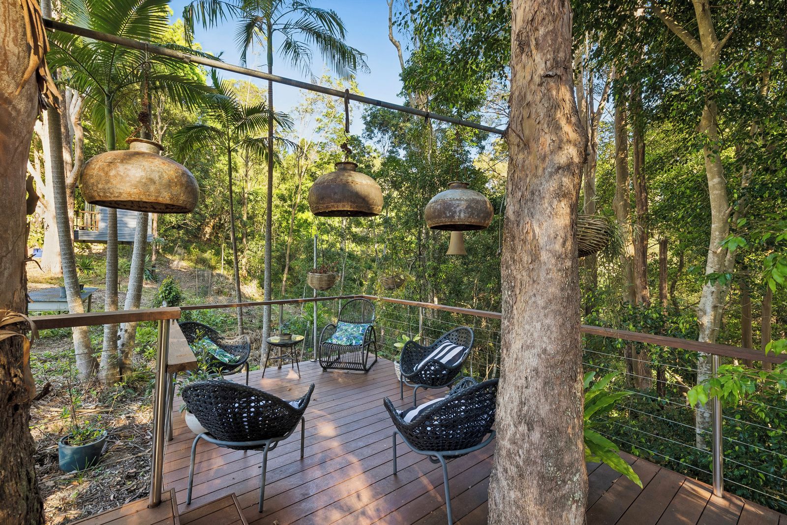 Una terraza exterior con suelo de madera, barandillas de metal y sillas de mimbre.