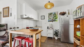 A modern kitchen with white cabinets, a wooden table, red bar stools, a stainless steel refrigerator, and a hanging light fixture.
