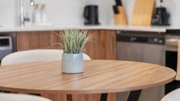 A round wooden table with a potted plant in the center, surrounded by white chairs.