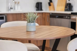 A round wooden table with a potted plant in the center, surrounded by white chairs. - Elegant Skyline Retreat | 2BR•UG Parking (Edmonton)