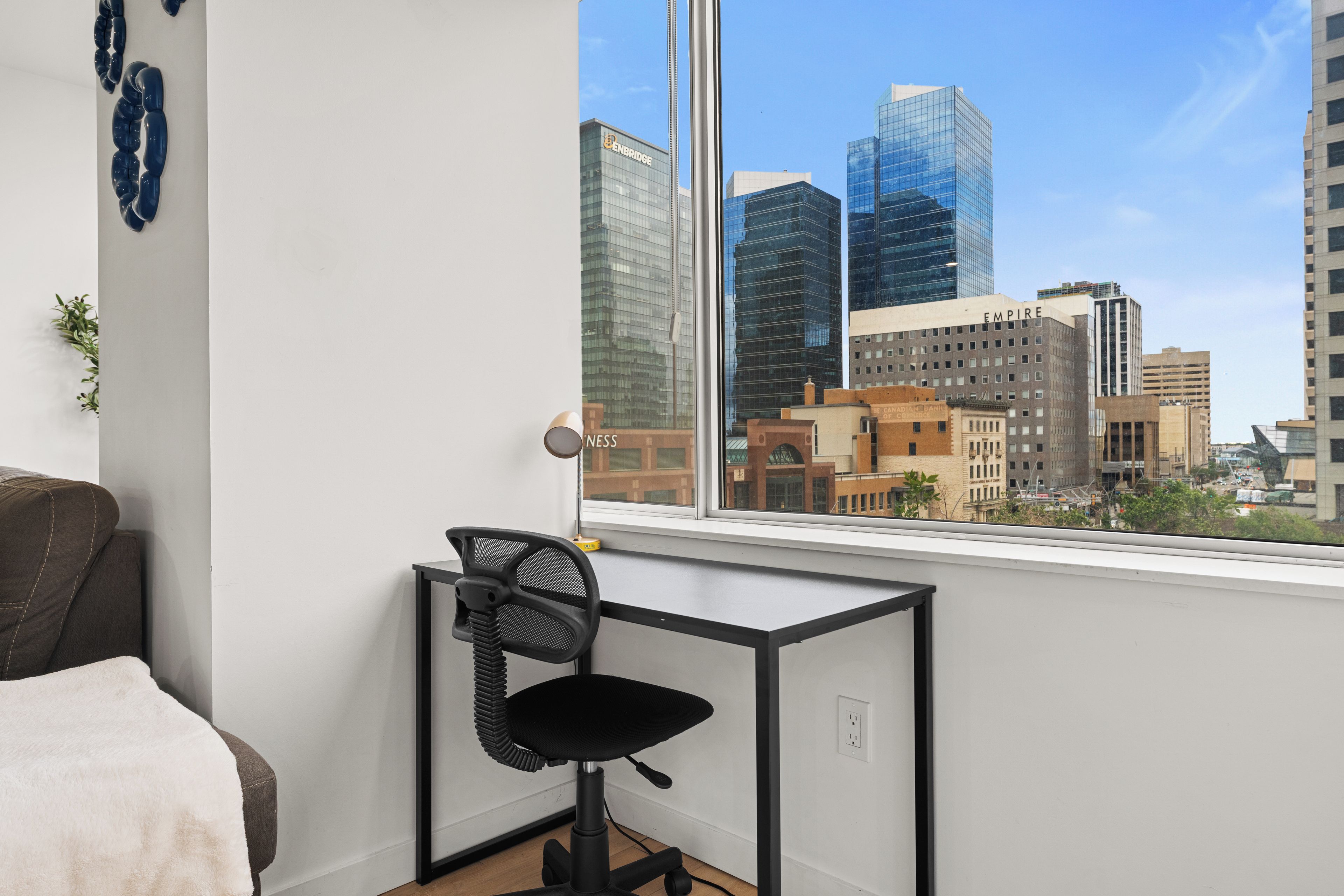 Un espacio de oficina moderno con un escritorio y una silla, un ventanal grande con vista a la ciudad, y una cama en la esquina.