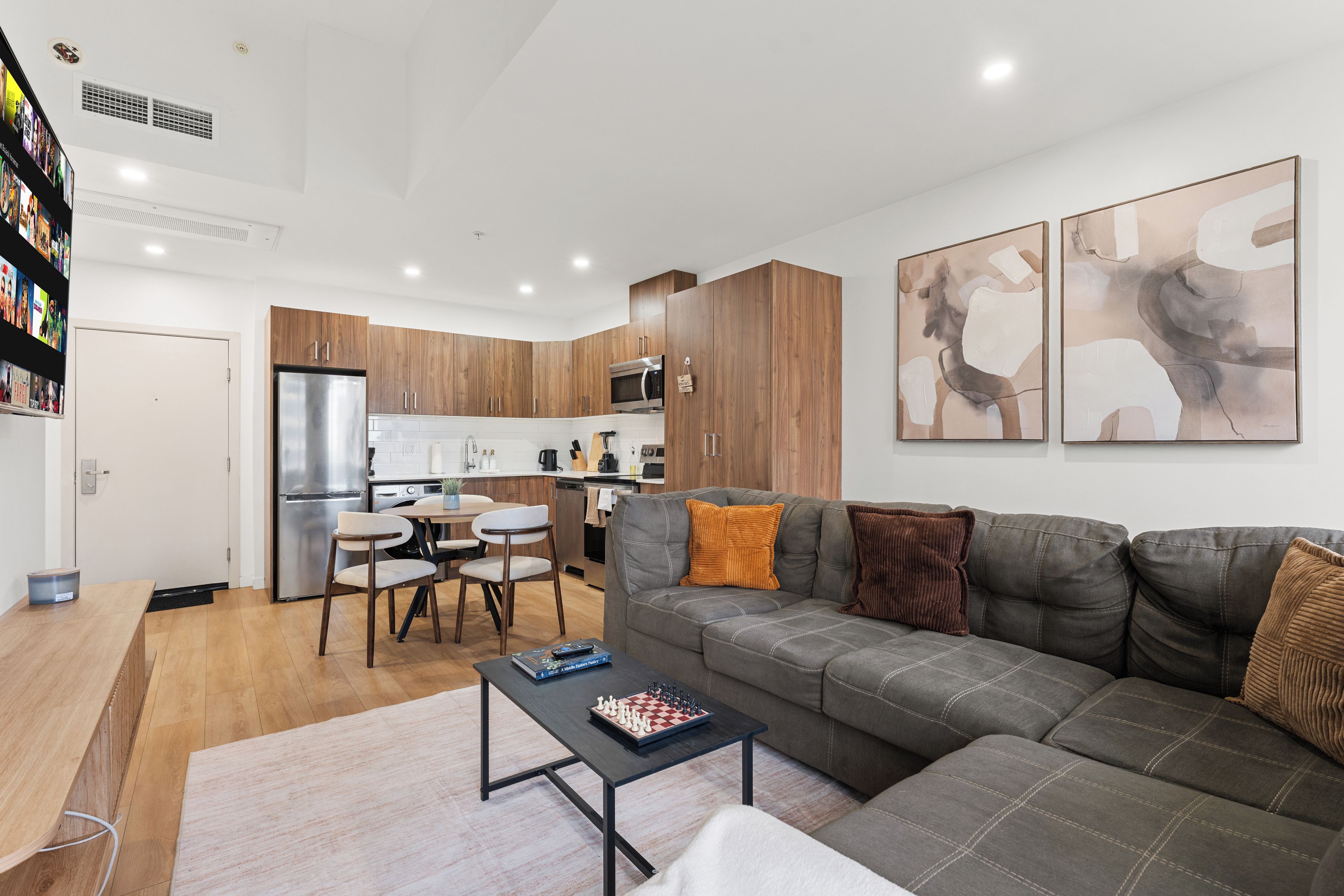 A modern living room with a grey sectional sofa, a coffee table, and a dining area with a white table and chairs.