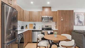A modern kitchen with stainless steel appliances, wooden cabinets, and a dining area with a round table and chairs.