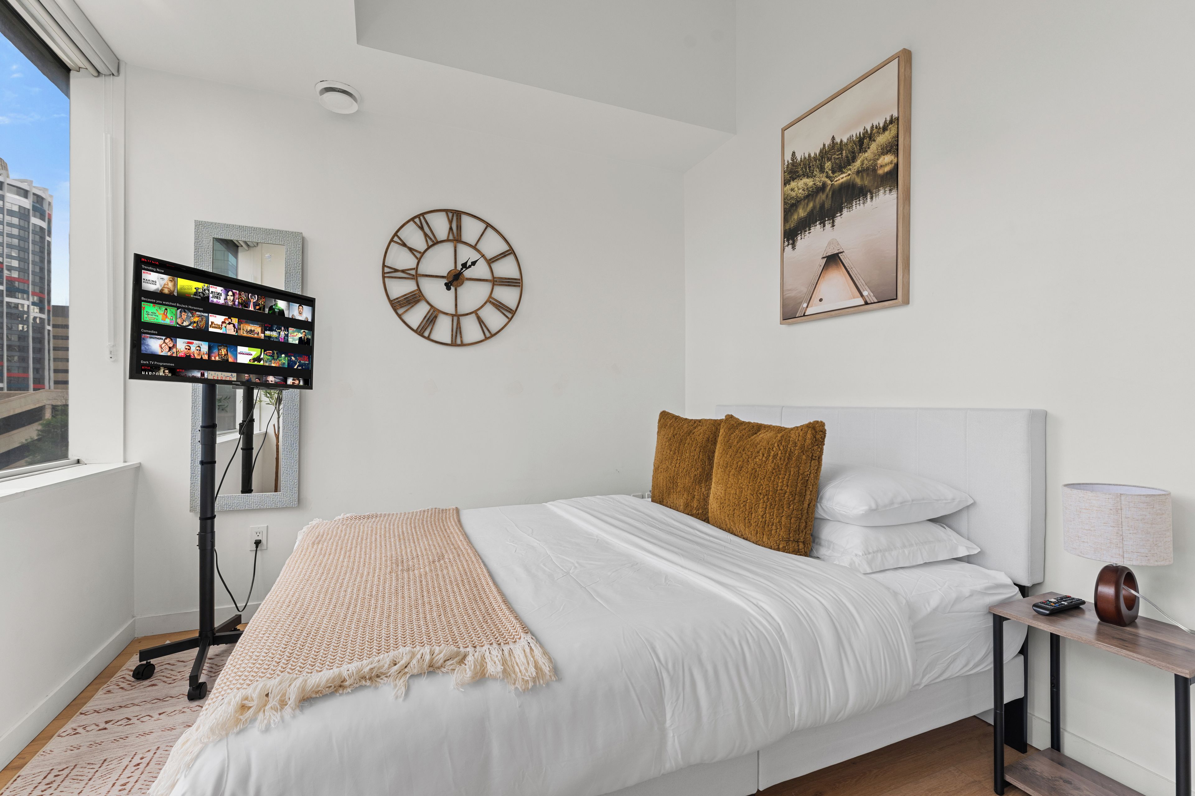 A modern hotel room with a bed, a TV, a clock, and a painting.