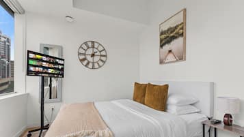 A modern hotel room with a bed, a TV, a clock, and a painting.