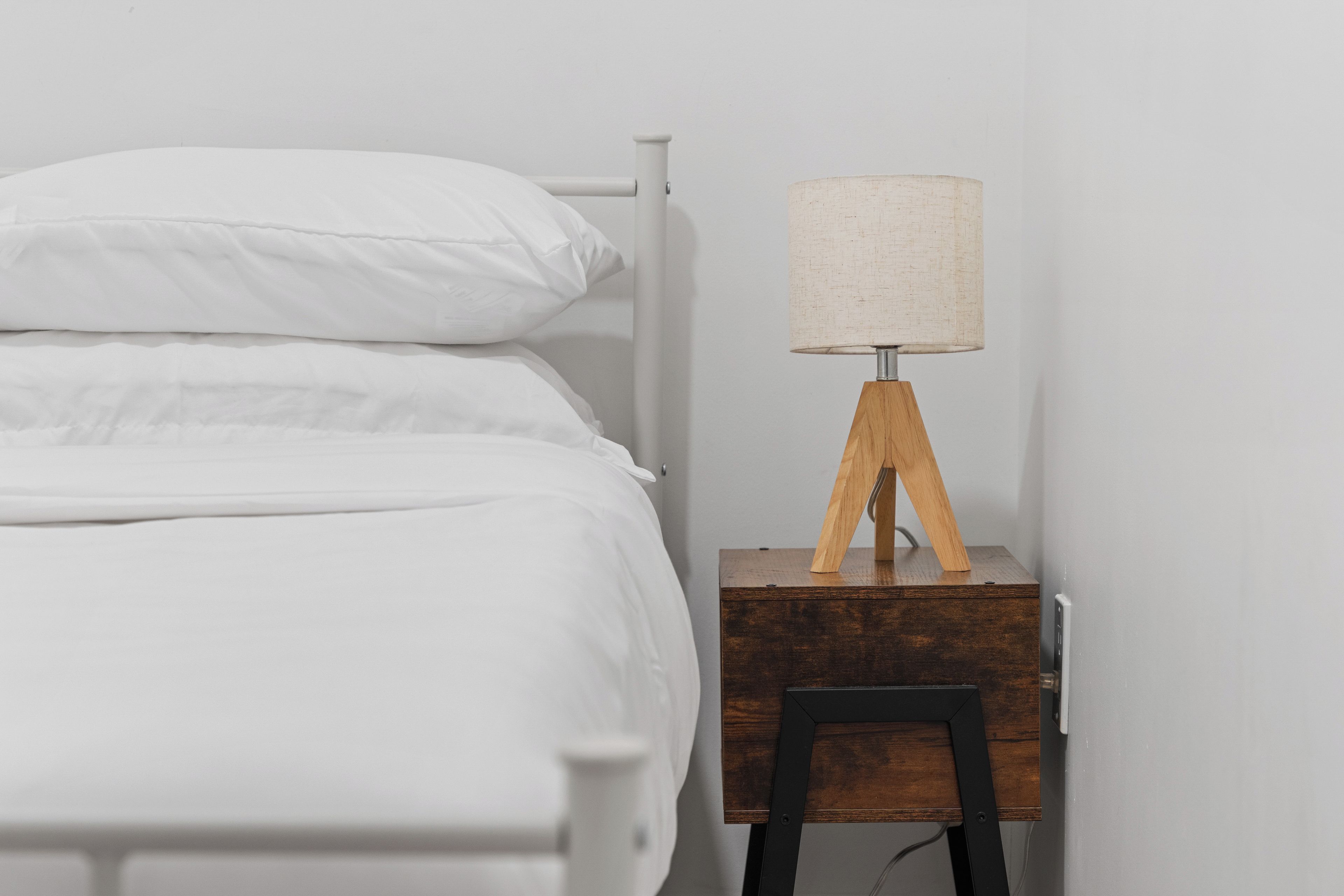 Una cama con ropa blanca y una mesita de noche de madera con una lámpara.