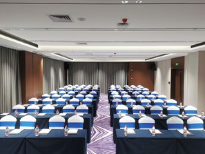 Une salle de conférence avec des rangées de tables, chacune étant équipée d’une bouteille d’eau et d’un bloc-notes.