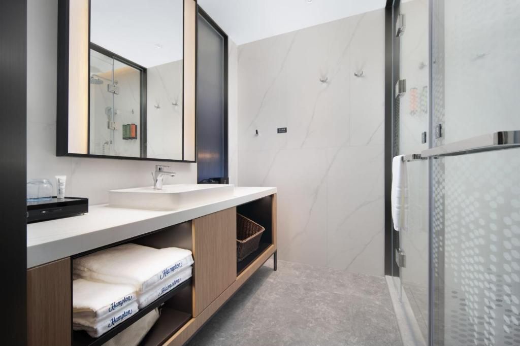 A modern bathroom with a large mirror, a sink, and a shower area.
