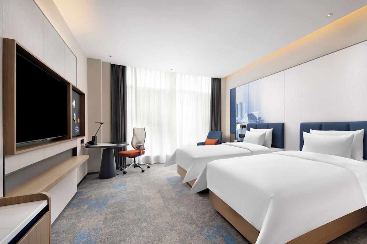 Een hotelkamer met een flatscreen-tv, een bureau, twee bedden en een groot raam.