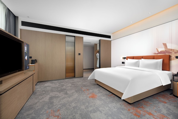 A hotel room with a large bed, a flat-screen TV, a wardrobe, and a bathroom visible through an open door.