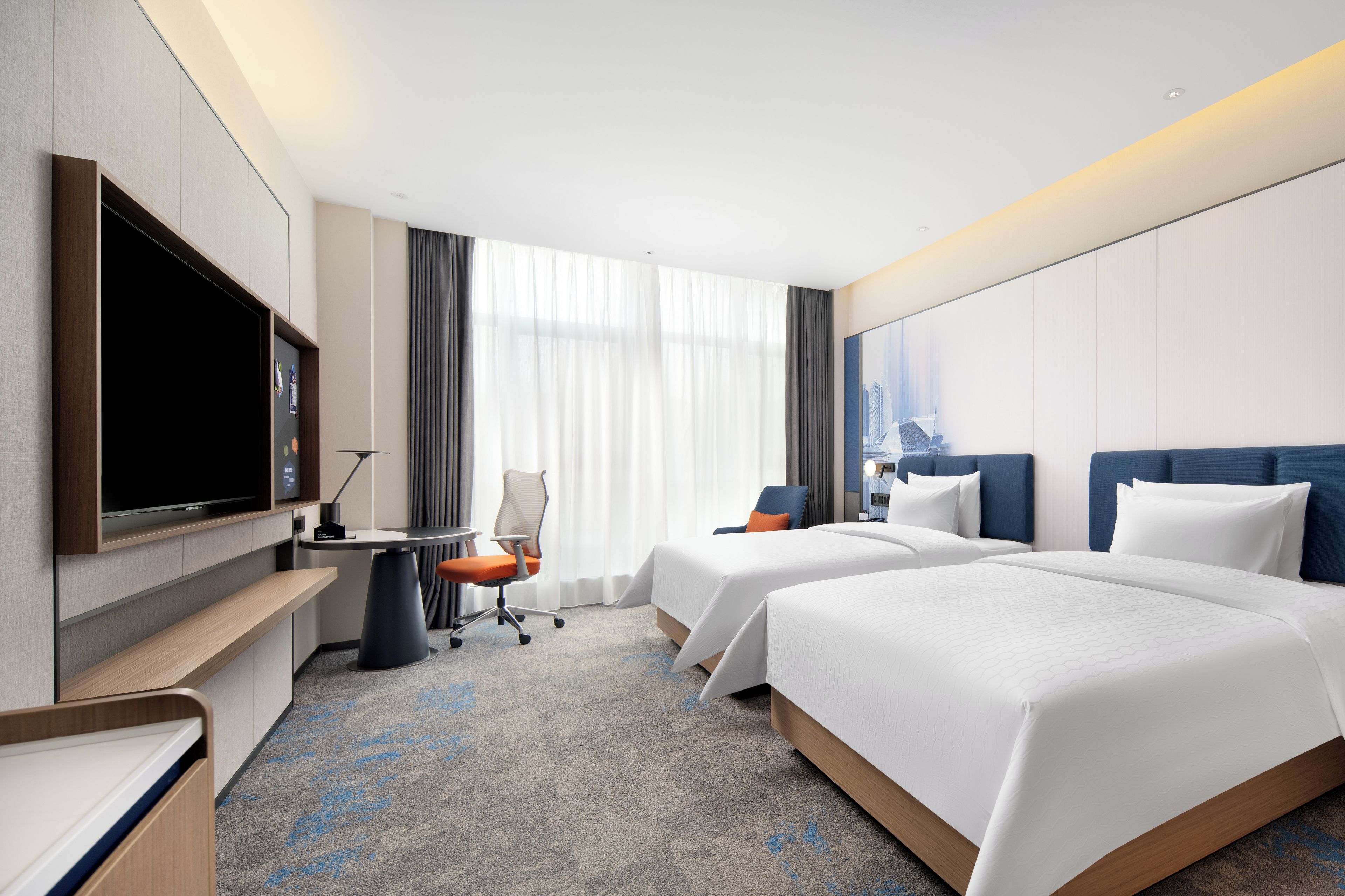A hotel room with two beds, a desk, a flat-screen TV, and a large window with curtains.