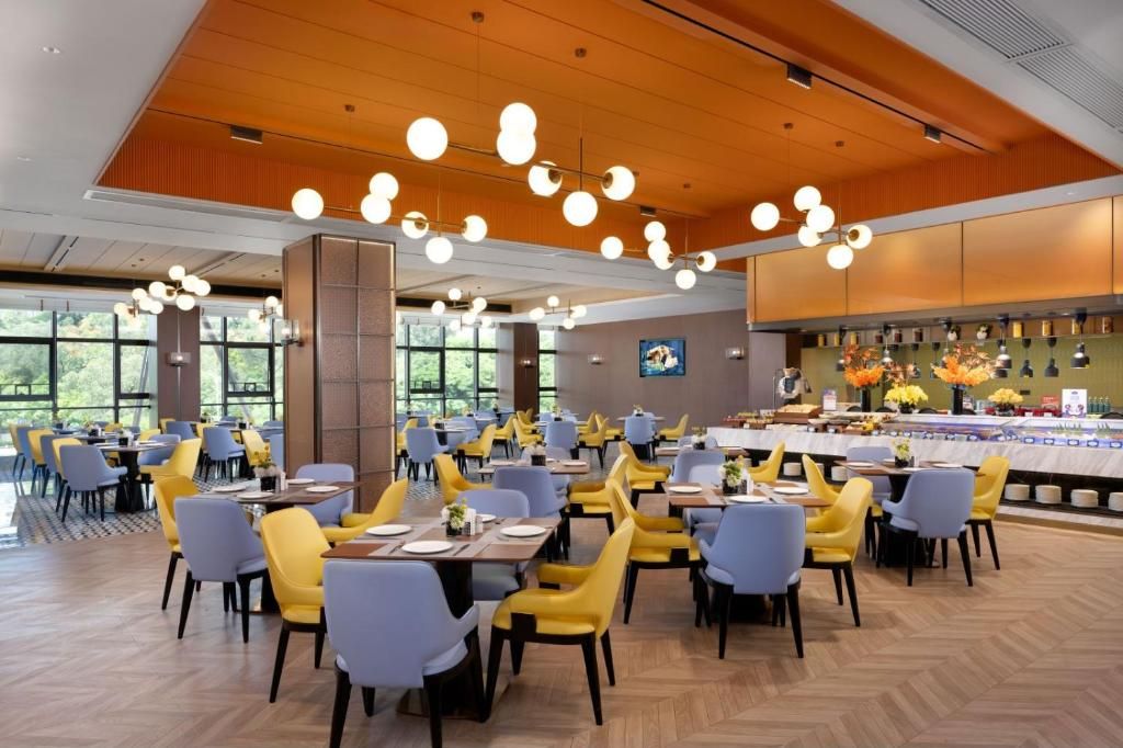 A spacious dining area with multiple tables and chairs, large windows, and a modern ceiling design.