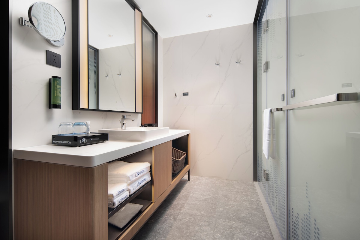 Ein modernes Badezimmer mit großem Spiegel, Waschbecken und einer Duschkabine aus Glas.