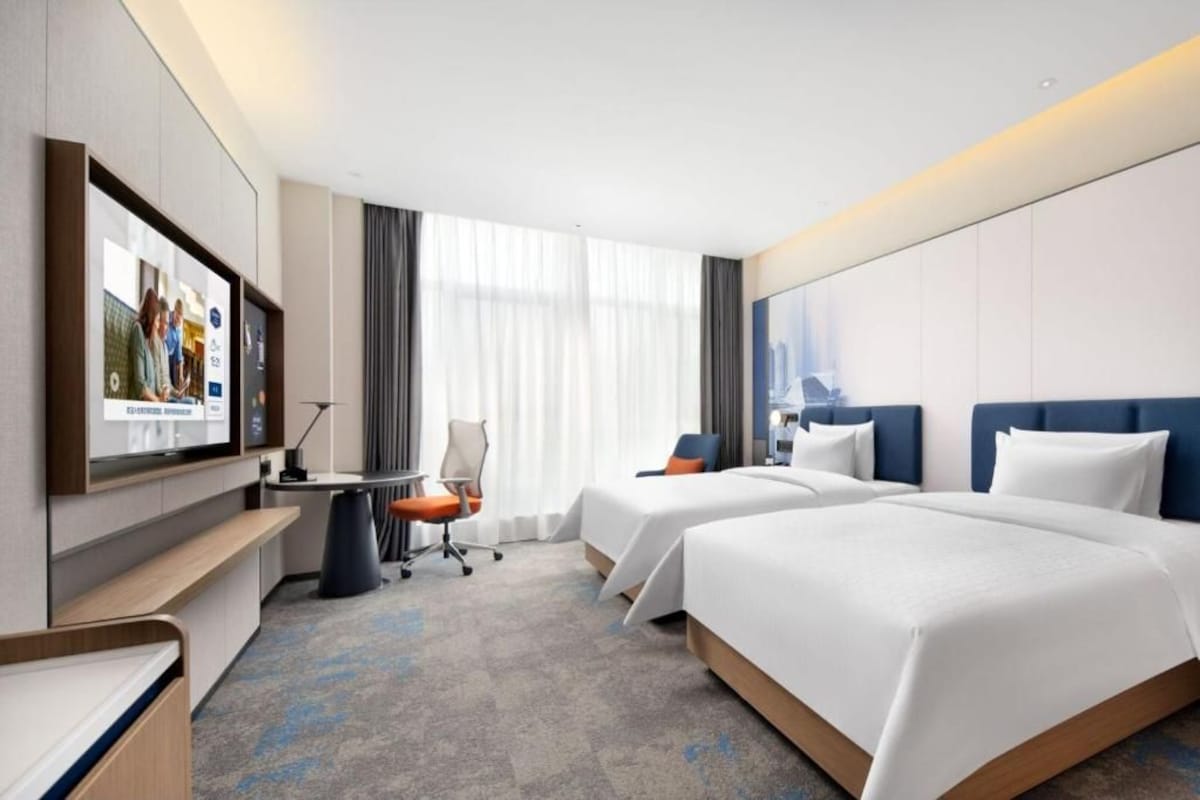 Habitación de hotel con dos camas, un escritorio, una silla y un televisor.