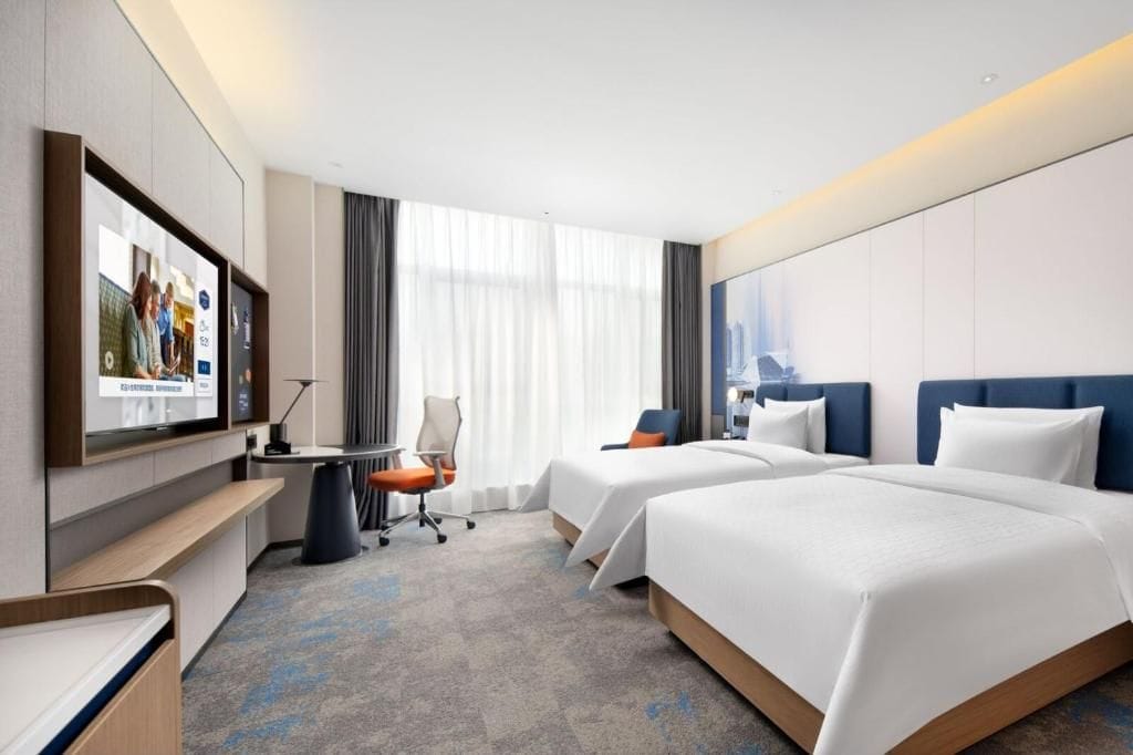 A hotel room with two beds, a desk, a chair, and a television.