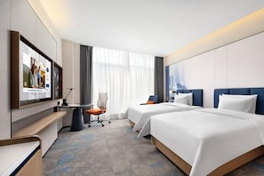 Habitación de hotel con dos camas, un escritorio, una silla y un televisor.