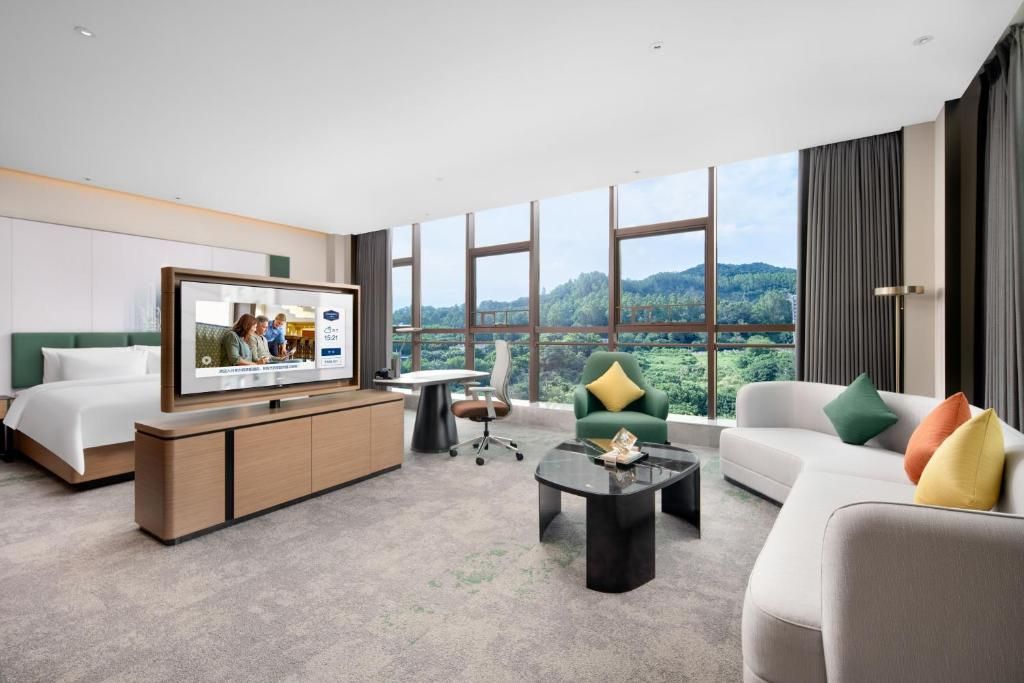Habitación de hotel con cama, televisor, sofá, mesa de centro y vistas al exterior.