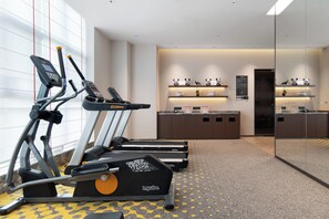 A hotel fitness center with treadmills, a wall-mounted mirror, and a reception area with a counter and decorative items.