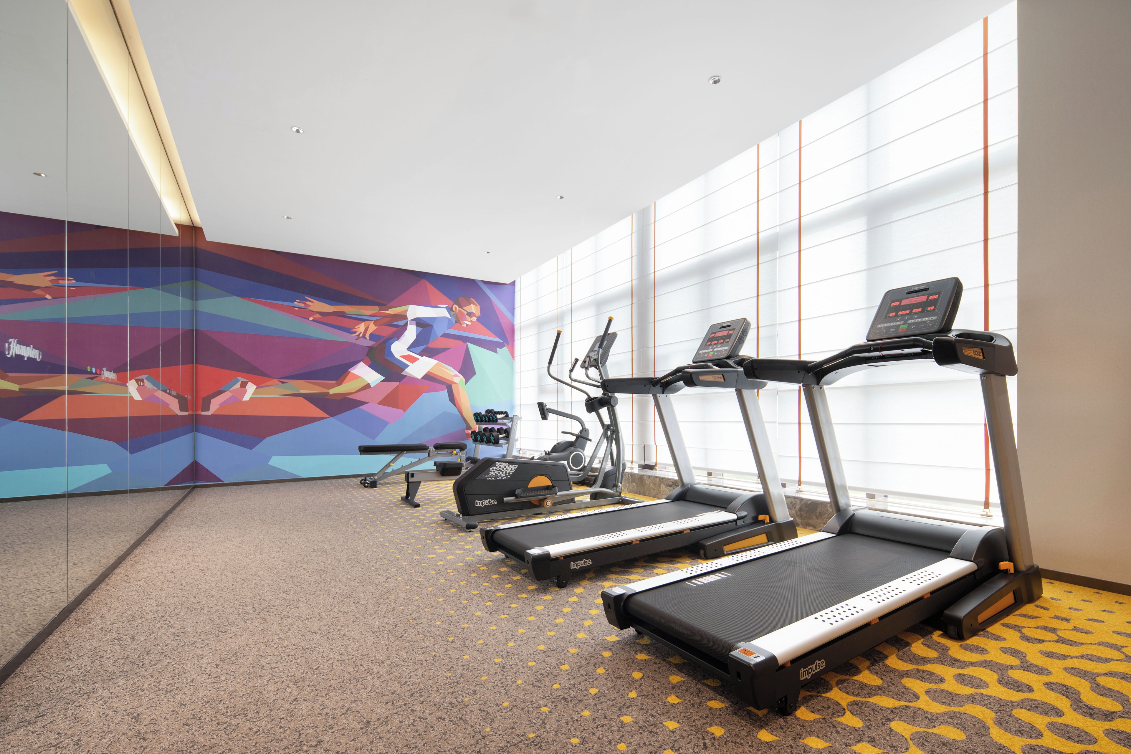 A gym with treadmills, dumbbells, and a colorful wall mural.