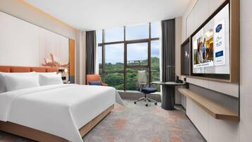 A hotel room with a large bed, a desk, a chair, and a TV mounted on the wall.