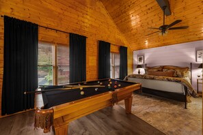 Ein gemütliches Zimmer mit Billardtisch, einem Bett mit floralem Bettzeug und einem Deckenventilator.