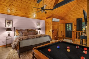 A cozy wooden cabin room with a bed, a pool table, and a ceiling fan. - 2Mi to Pkway|Hot Tub|Newly Renovated|LUXE Cabin (Pigeon Forge)
