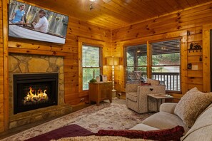 A cozy cabin interior with a stone fireplace, a television mounted on the wall, and a comfortable seating area with a sofa and a small table. - 2Mi to Pkway|Hot Tub|Newly Renovated|LUXE Cabin (Pigeon Forge)