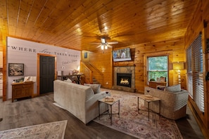 A cozy cabin interior with a fireplace, wooden walls, a sofa, and a television. - 2Mi to Pkway|Hot Tub|Newly Renovated|LUXE Cabin (Pigeon Forge)