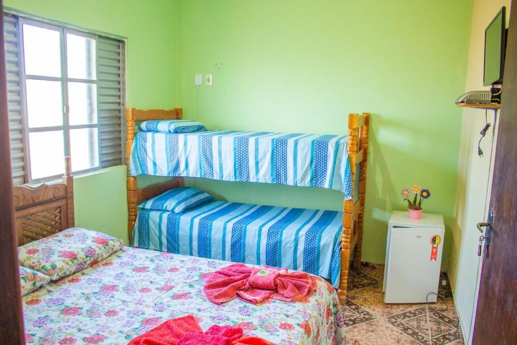 A room with a bunk bed, a single bed, a small refrigerator, and a window with blinds.
