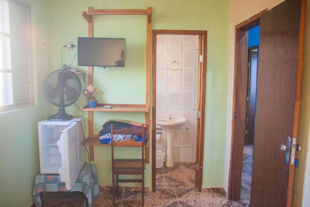 Habitación pequeña con televisión, ventilador, una silla, una mesita y un lavabo.