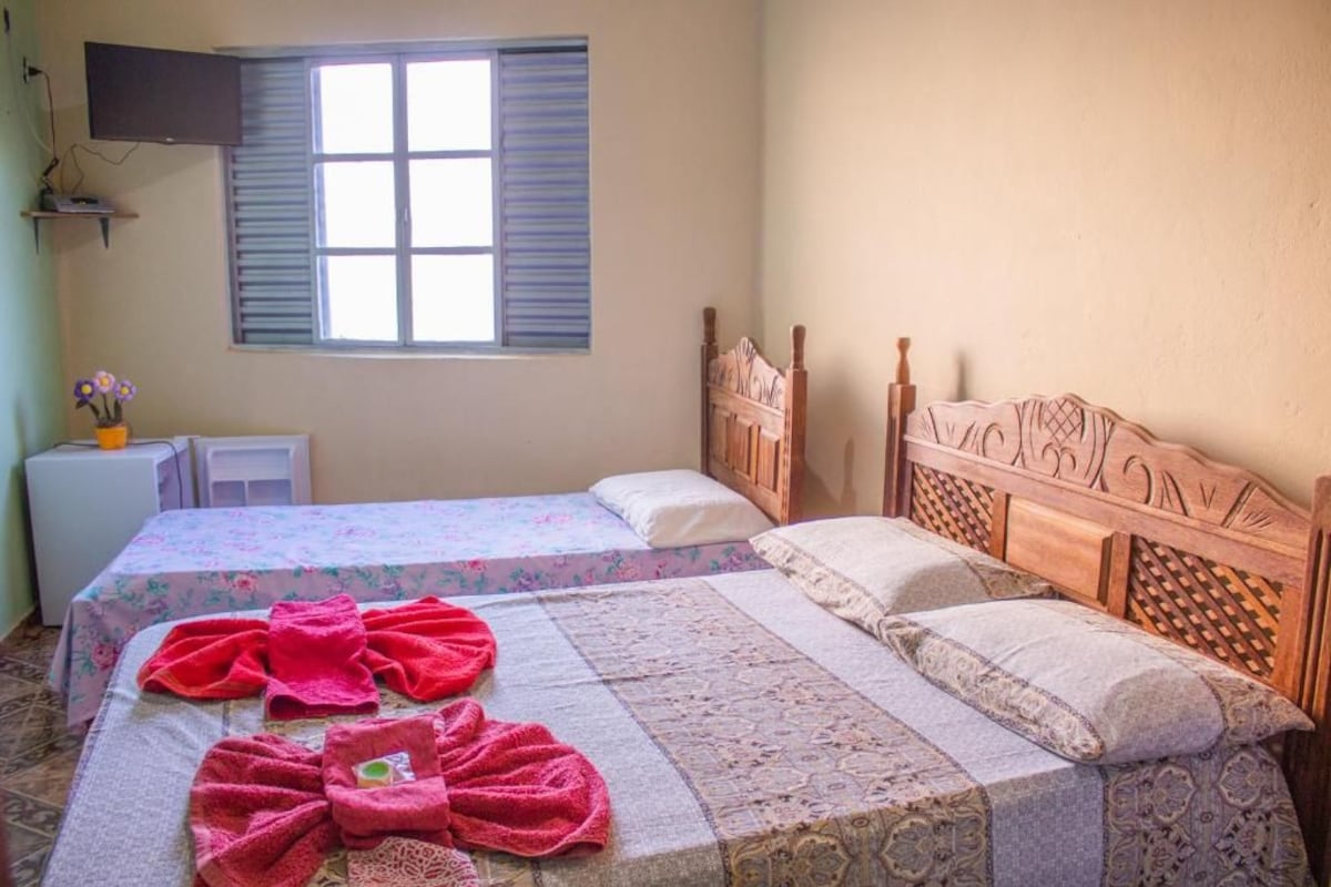 Une chambre avec deux lits, un téléviseur fixé au mur et une fenêtre avec des volets.