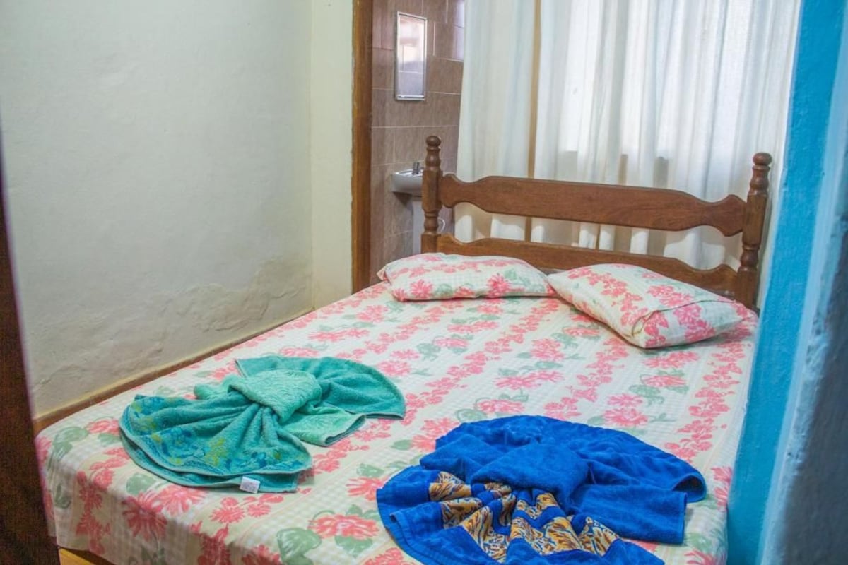 A single bed with floral bedding, a wooden headboard, and a window with curtains.