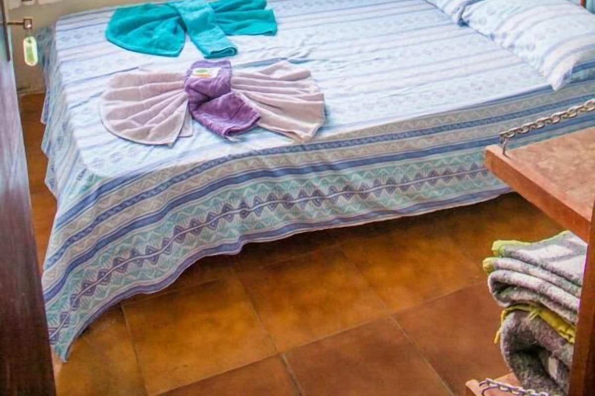 Un lit simple avec une couvre-lit à motifs, une tête de lit en bois et une fenêtre avec des rideaux.