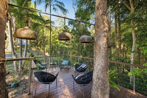 An outdoor deck with seating and hanging planters, surrounded by trees. - Studio Jindi - Jindi- Bundjalung word for “a safe & creative nest amongst the trees” (Nunderi)