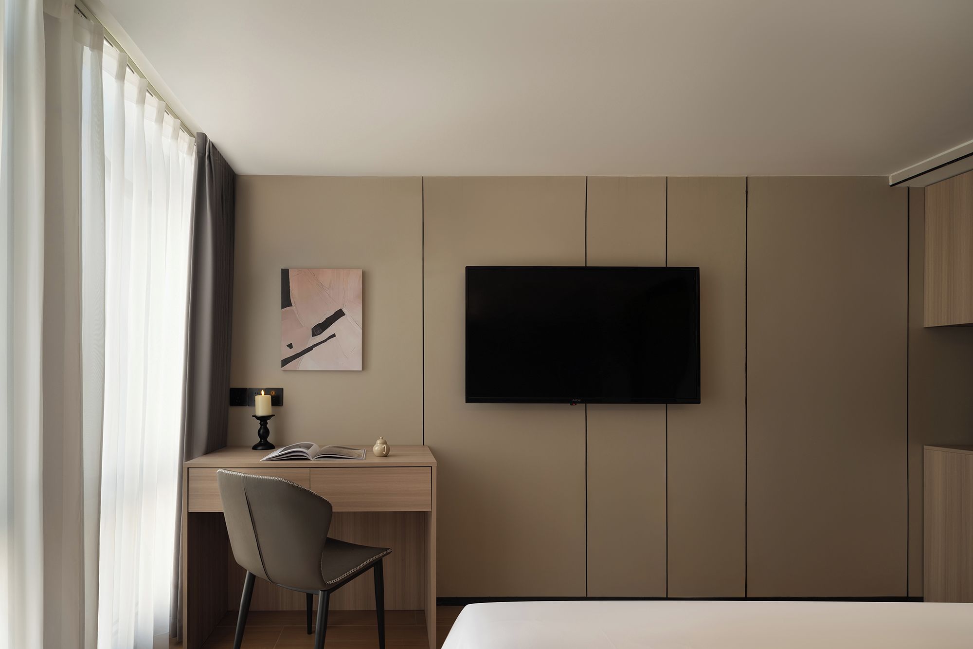 A hotel room with a bed, a desk with a chair, a television mounted on the wall, and a window with curtains.
