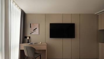 A hotel room with a bed, a desk with a chair, a television mounted on the wall, and a window with curtains.