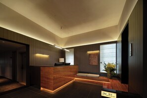 A modern reception area with a wooden reception desk, a seating area, and a large window providing natural light.