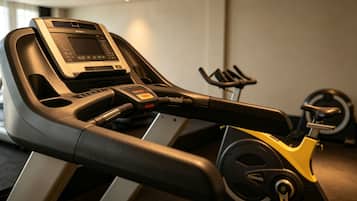 A stationary bike with a digital display and control panel, positioned in a room with a treadmill and a wall-mounted exercise equipment.