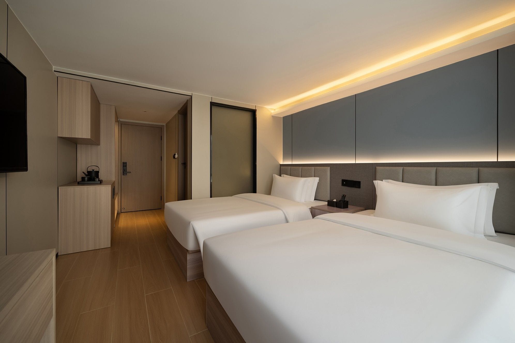 A hotel room with two beds, a flat-screen TV, a bedside table, and a wardrobe.