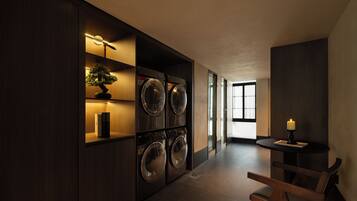 A laundry room with multiple washing machines, a small table with a candle, and a bonsai tree on a shelf.