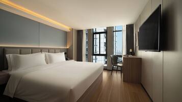 Habitación de hotel con una cama grande, un escritorio, una silla, un televisor y una ventana con vista a la ciudad.