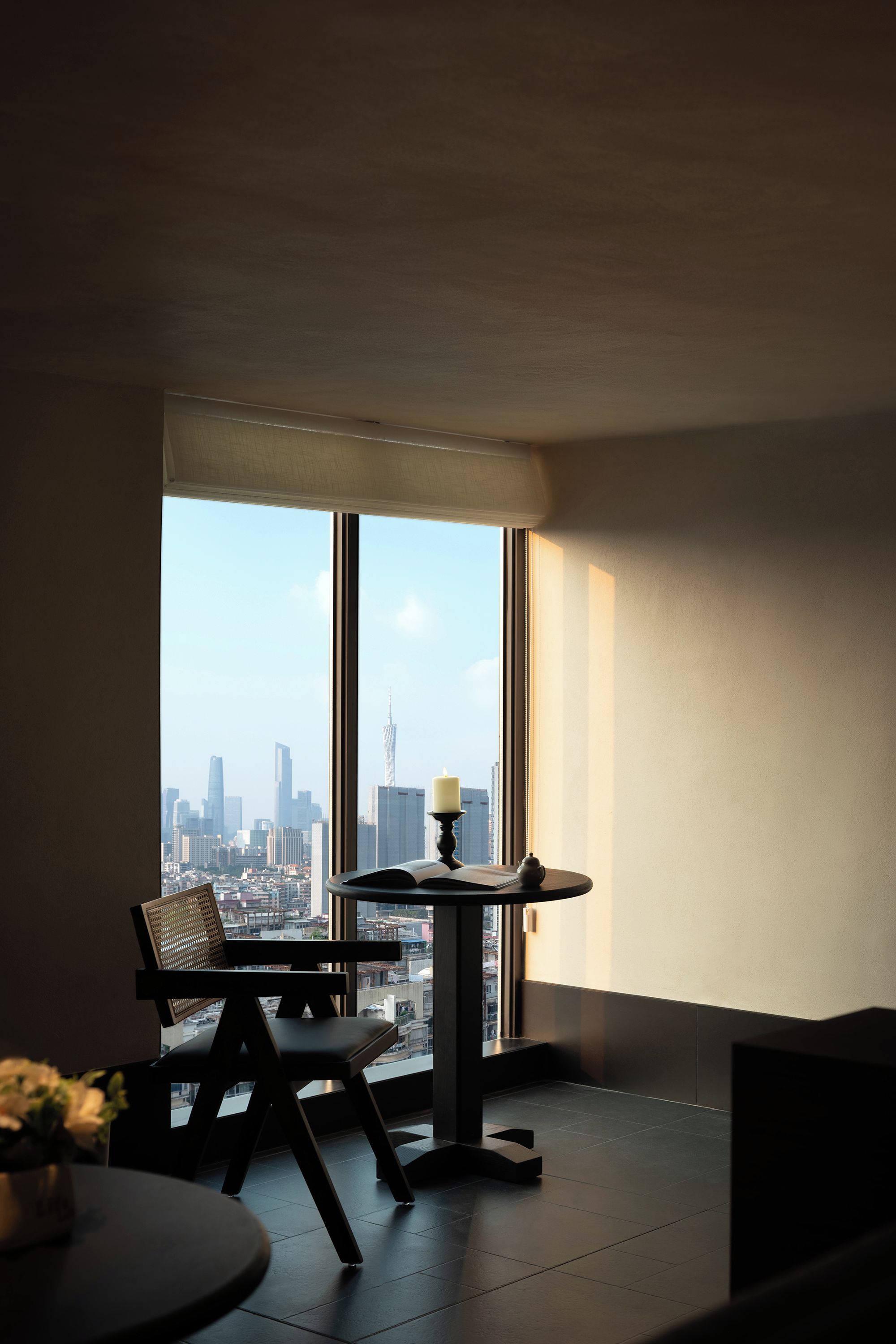 A room with a large window, a chair, a small table, and a view of a cityscape.
