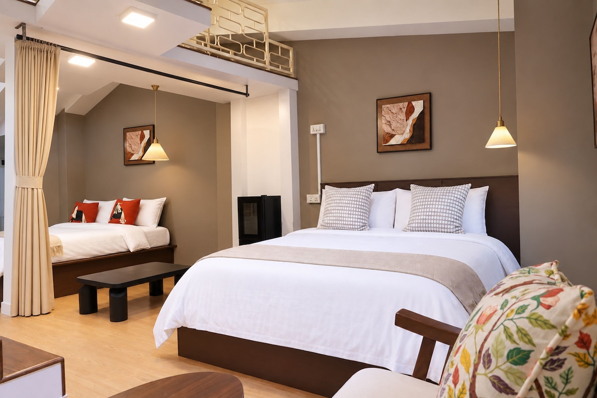 A hotel room with a large bed, a smaller bed, a bench, a desk, and a chair.