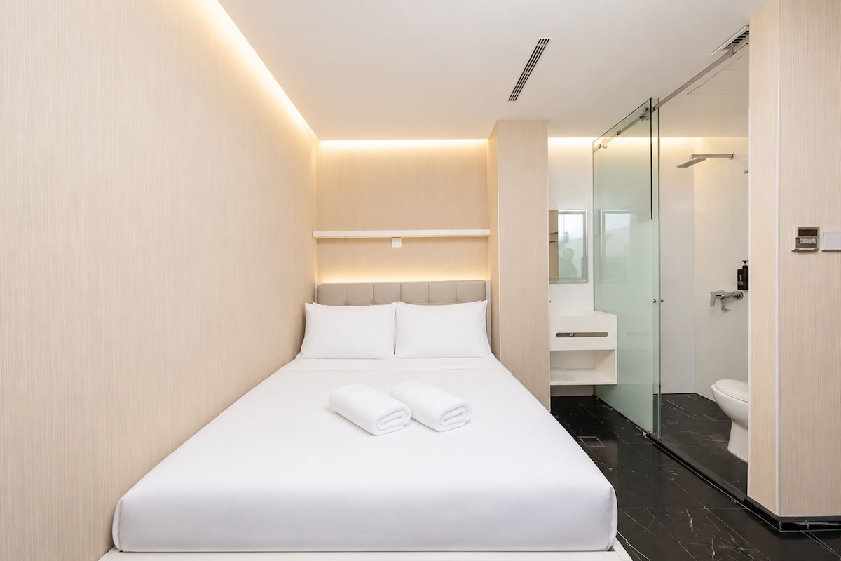 A modern hotel room with a neatly made bed, a glass shower enclosure, and a minimalist bathroom design.