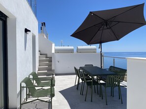 An outdoor patio with a table and chairs, a large umbrella, and a view of the sea. - Penthouse in Malaga With Sea View Terraces (Nerja)
