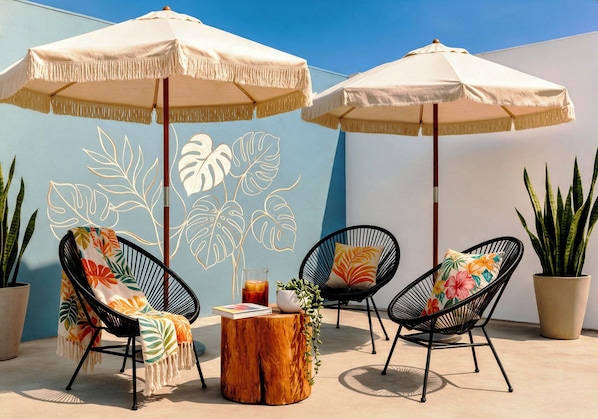 An outdoor seating area with two chairs, a wooden table, and two umbrellas. - 2 Suites · 4 Beds Sleeps 8 · WiFi AC · 5th Ave, ADO, Beach, Cozumel Ferry 4 Mins (Playa del Carmen)