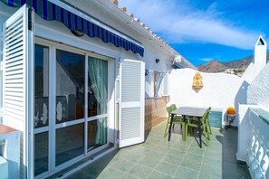 A coastal property with a patio area featuring a table and chairs, a sliding glass door, and a decorative wall with a lion head. - Apartment in Nerja Near Burriana Beach (Nerja)