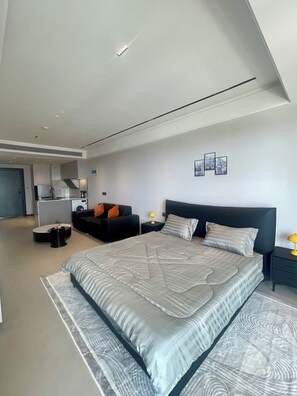 A modern bedroom with a large bed, a dark headboard, and a small bedside table with a lamp.