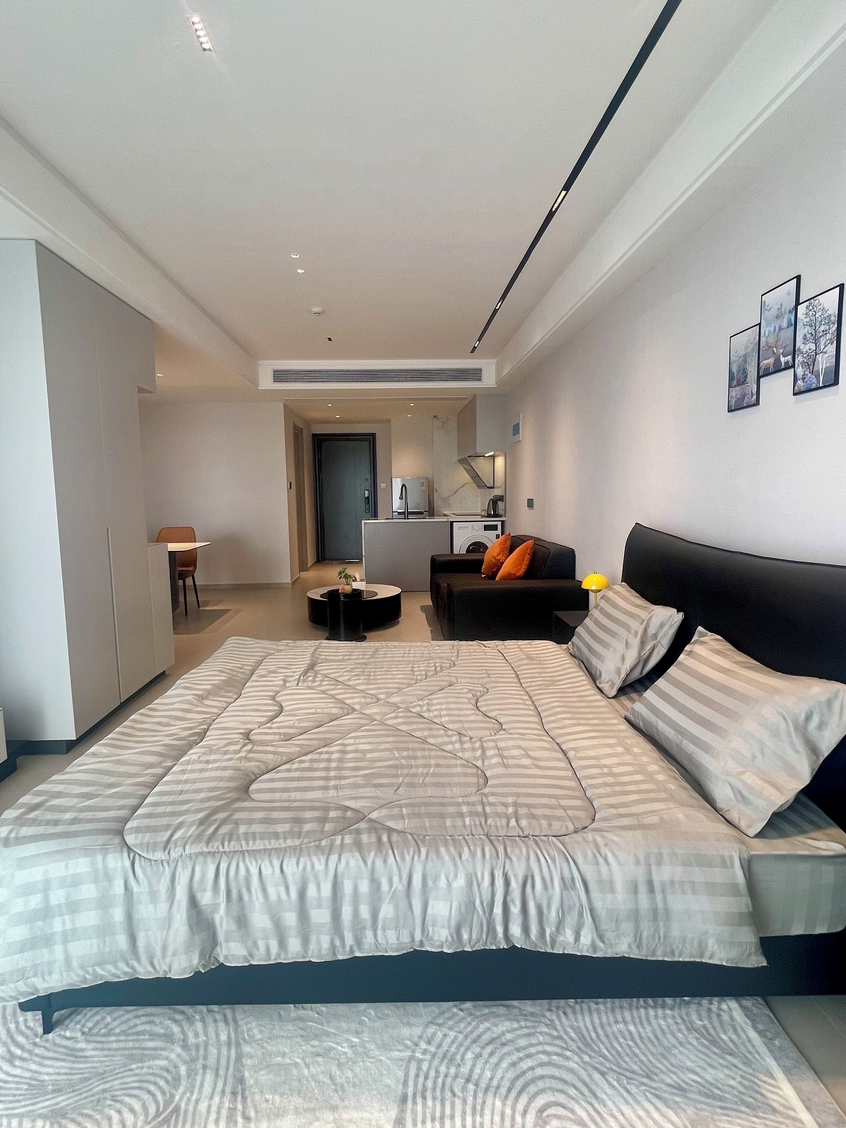 Une chambre moderne avec un grand lit, un canapé, un coin repas et une cuisine en arrière-plan.
