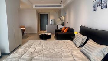 Une chambre moderne avec un grand lit, un canapé, un coin repas et une cuisine en arrière-plan.